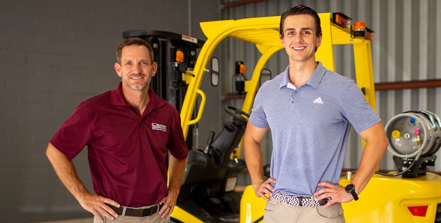 Two men standing in front of a Hyster lift truck smiling.