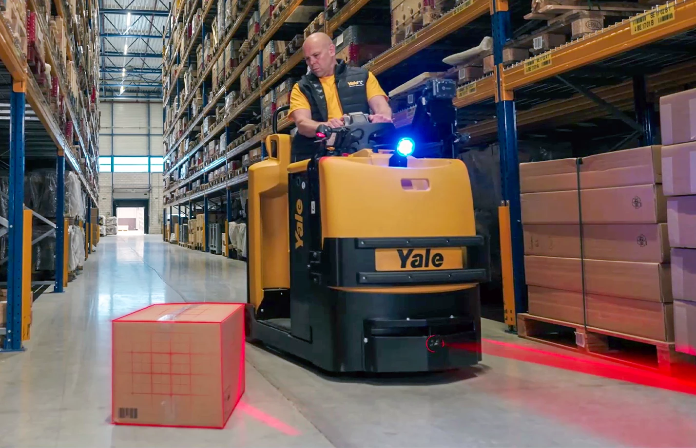 Operator driving a Yale tow tractor in a warehouse with graphics illustrating Yale Reliant object detection.