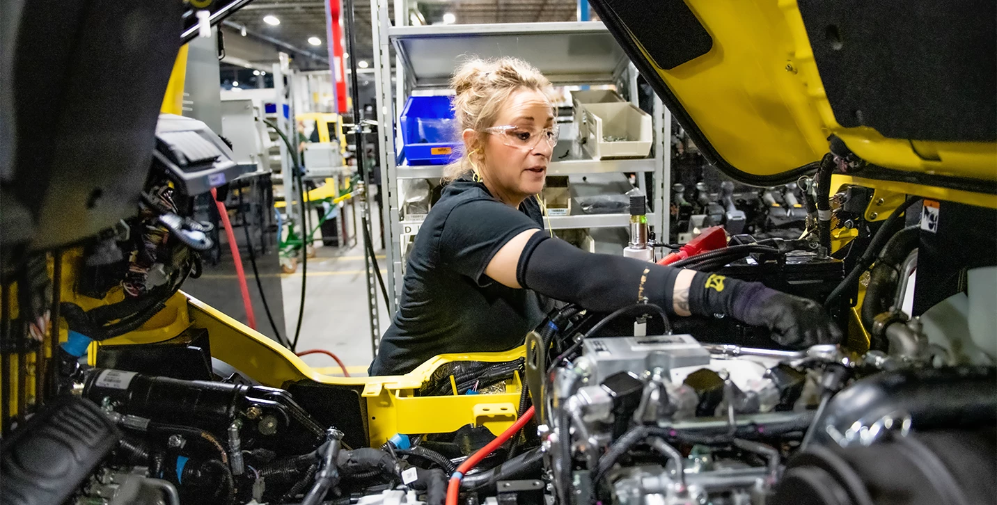 Woman completing final forklift inspection in manufacturing plant. 