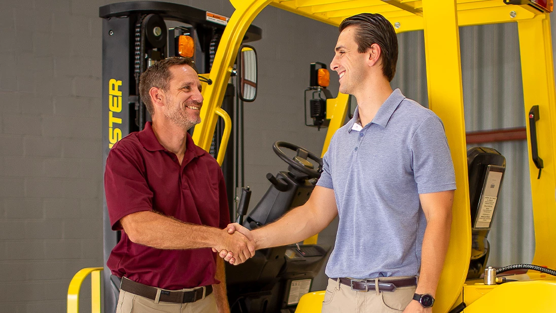 Two men shaking hands in front of a Hyster forklift. 