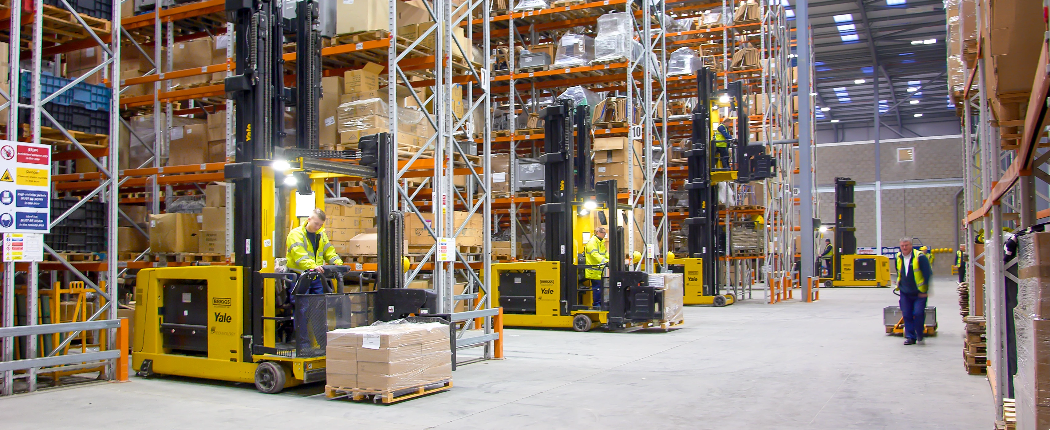 Numerous Yale turret trucks working in narrow warehouse aisle.