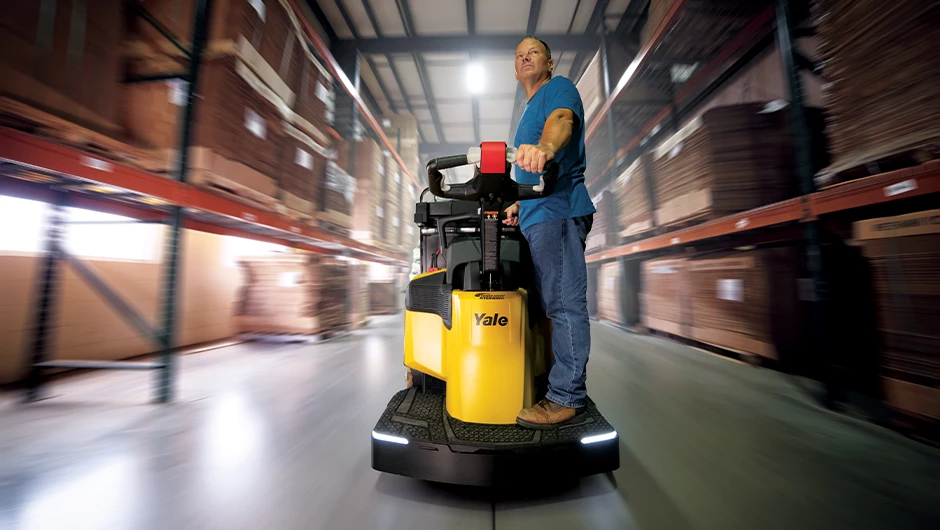 Person transporting loads on Yale rider pallet truck in warehouse. 