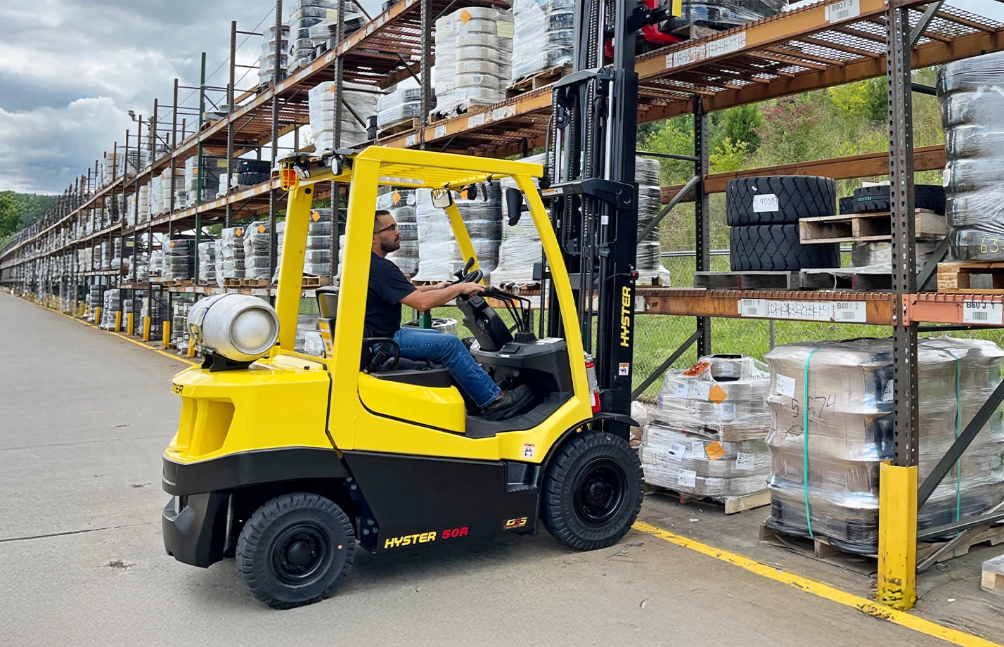 An operator using a Hyster forklift to remove a pallet of products from an industrial shelving unit.